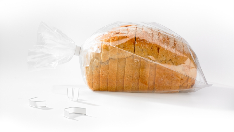 Opakowanie z chlebem zamknięte klipsem clipband i białe U-klipsy leżące przed nim